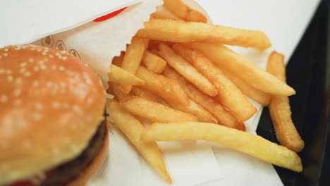 patatas fritas doradas y una hamburguesa en una bandeja negra con una mano alcanzando para elegir una. vista de cerca