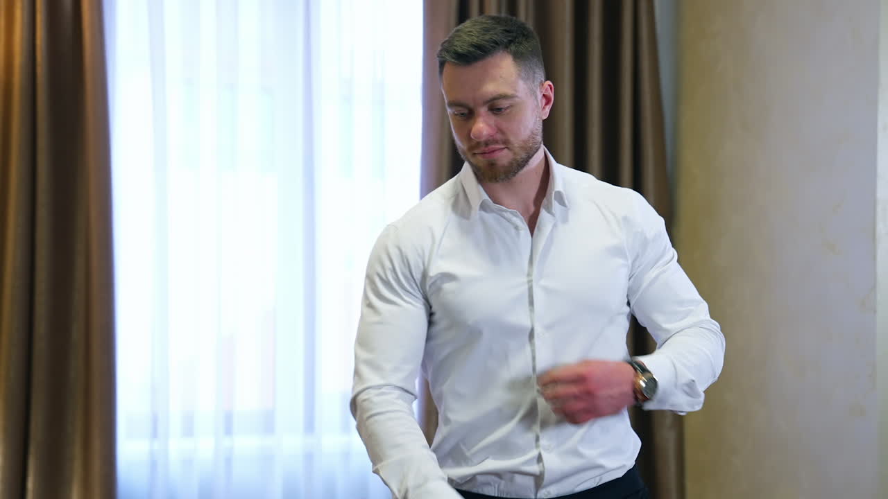 Successful businessman near the window. Handsome man in white shirt at modern room in a hotel. Bearded young man on the background of luxury curtains.