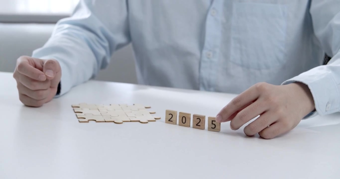Close-up of an office worker’s hand changing year from 2024 to 2025 using wooden numbers and jigsaw, a visual representation of annual success planning and business goal setting