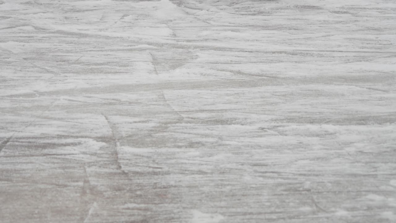 Primer plano de patines de hielo deslizándose sobre una superficie helada rayada. Las afiladas cuchillas se mueven rápidamente sobre el hielo blanco texturizado durante una sesión de patinaje al aire libre.