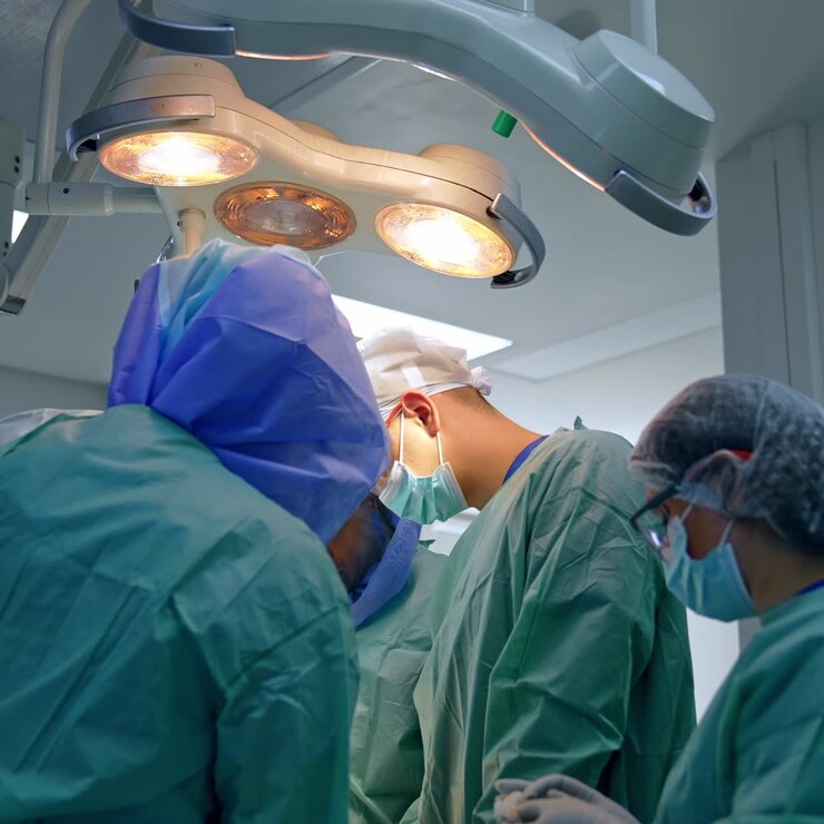Four surgeons stand around the patient carrying out the operation. Female nurse assisting at trauma surgery