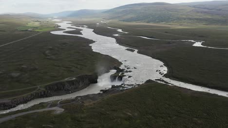 meandering glacier water river with view of goðafoss waterfall, aerial