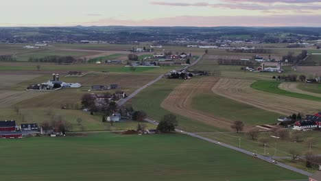 traffic on intersection road in rural area of north carolina with colorful agricultural fields in winter. farms with silo and stable in usa. aerial wide shot. sunset time.
