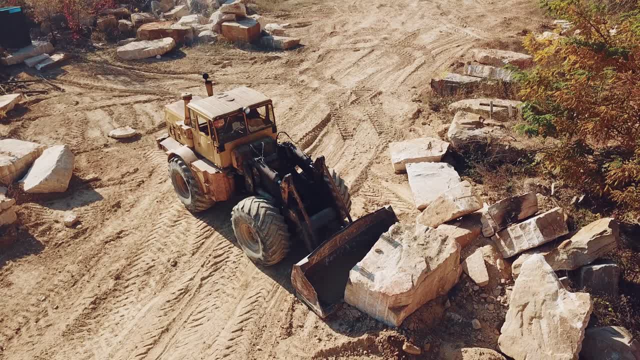 professional equipment with a bucket is turning over a stone and raising it near sandy quarry on the background of trees. Close-up