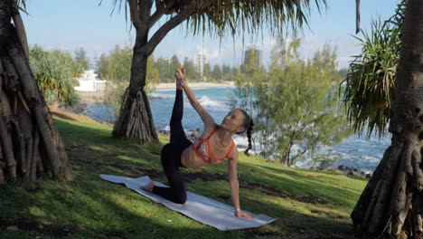 mujer delgada haciendo pose de tigre en una alfombra - yoga en la playa - playa de burleigh heads en queensland, australia