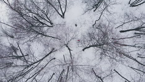 Aerial:-Man-and-woman-running-through-woods-in-winter-time