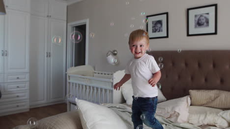 a boy in a white t-shirt and blue jeans catches soap bubbles standing on the bed in the parent bedroom