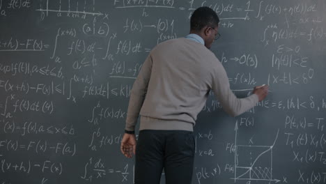 man writing equations on a blackboard