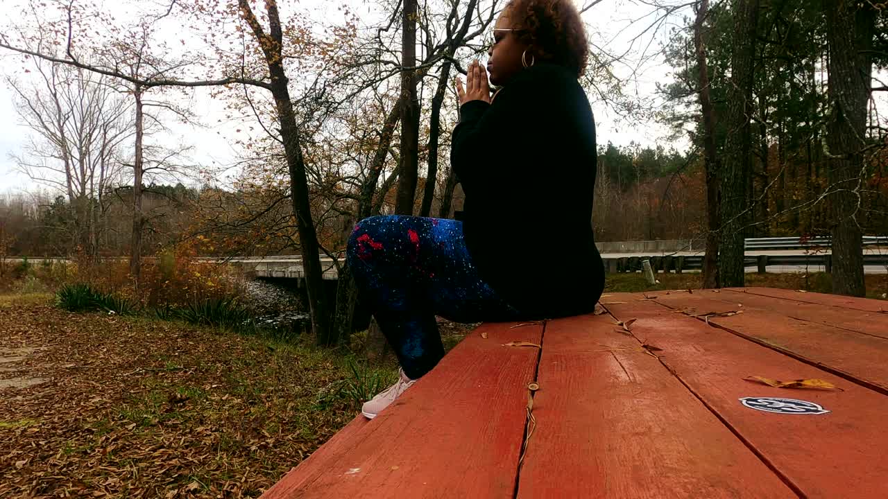 joven negra reza en un banco del parque en un día nublado