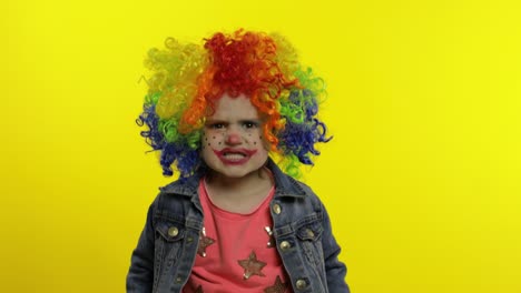 angry little child girl clown in colorful wig making evil faces. having fun. halloween. expressions