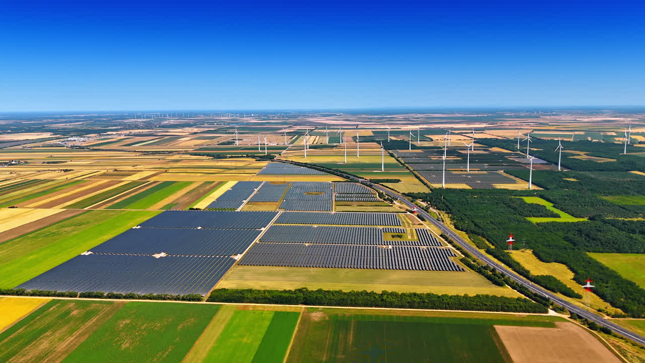 Solar panels accumulating sunlight in the countryside. Wind farms produce clean energy at backdrop. Aerial view
