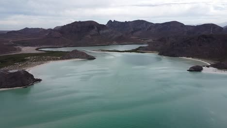 Playa-balandra-with-turquoise-waters-and-mountain-backdrop-in-baja-california,-mexico,-during-daylight,-aerial-view