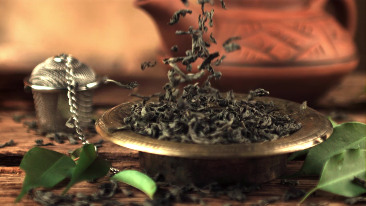 Dried Green Tea Leaves Falling into a Golden Bowl in Slow Motion