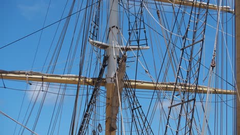 tall ship rigging gently swaying, frontlit against a blue sky and few clouds