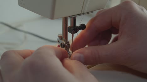 una vista estática de cerca de las manos enhebrando la aguja en una máquina de coser en un ambiente silencioso con muy poca cantidad de color