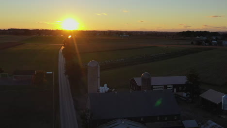 reverse drone shot that reveals a farmhouse and grain silos during a surreal sunset