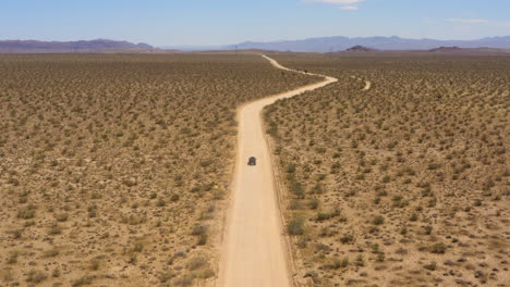 suv negro se acerca a una curva en un camino recto a través de las llanuras en el desierto de mojave en un día azul claro