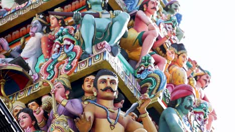 camera pans upward along a vibrant, intricately decorated hindu temple gopuram, revealing colorful deities and figures in bright daylight with clear sky