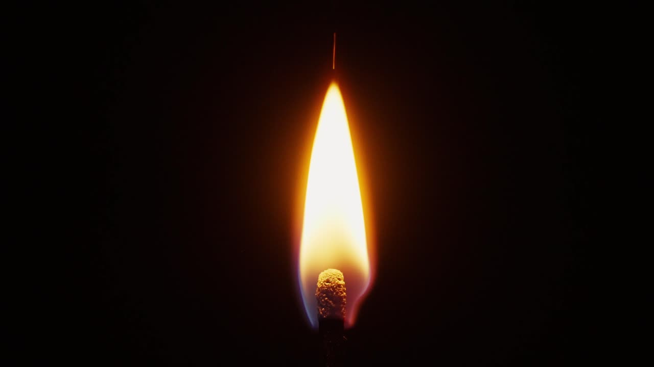 slow motion macro shot of a match head igniting and then burning on a black background