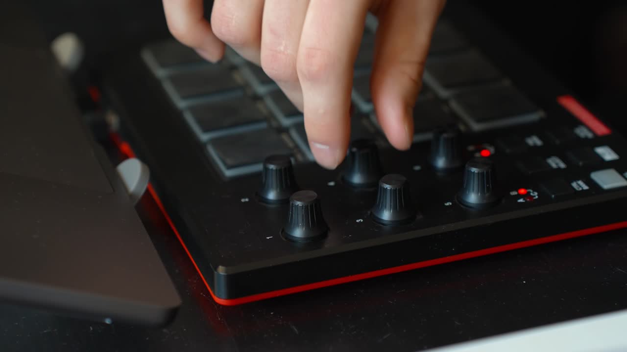 Hand turns a control knob on an FX sound MIDI pad controller, demonstrating sound design and electronic music production with acoustic guitar recording in a complete, laptop-based home studio setup