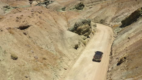 Large-black-SUV-drives-slowly-and-carefully-down-a-dirt-road-cutting-through-the-mountains-in-the-Rainbow-Basin-in-the-Mojave-Desert