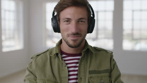 Primer-Plano-Retrato-De-Un-Joven-Atractivo-Sonríe-A-La-Cámara-Se-Pone-Auriculares-Escuchando-Música-Disfrutando-De-Actividades-De-Ocio-En-El-Apartamento