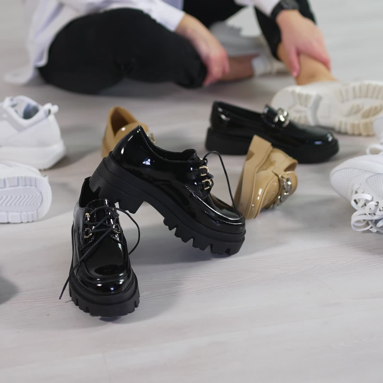 Woman sits on the floor surrounded by new fashionable footwear. Lady rejects all shoe variants choosing the black lacquered ones