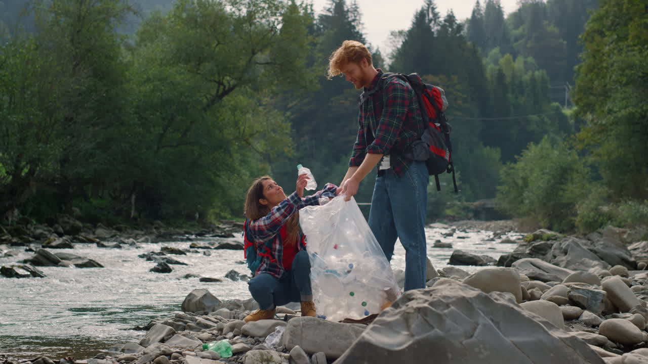 excursionistas limpiando la orilla del río de plástico. hombre y mujer alegres recogiendo basura