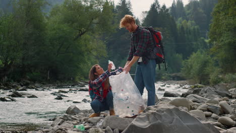 hikers cleaning river shore from plastic. joyful man and woman picking trash