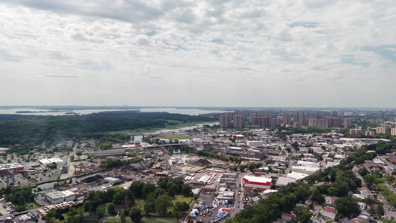 Imagens aéreas amplas mostrando a paisagem urbana do Bronx em Nova Iorque, com casas residenciais, áreas industriais e edifícios de apartamentos altos sob um céu parcialmente nublado