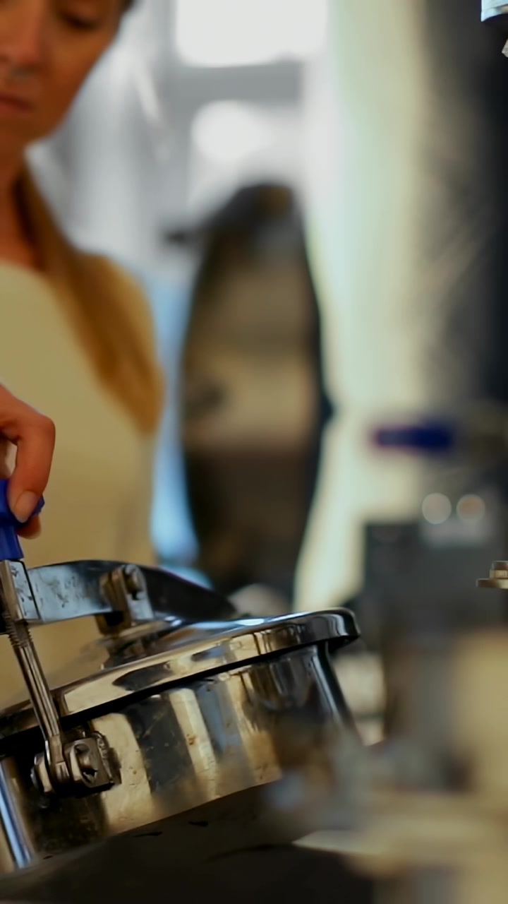 Video verticale: Mano che entra, donna in top che usa una pinza blu su un coperchio in cucina mentre controlla, con spazio per il testo.