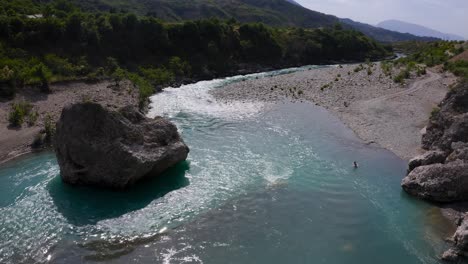 aerial view of solo man bathing in fresh flowing waters of of vjose river enjoying picturesque sight of mountains