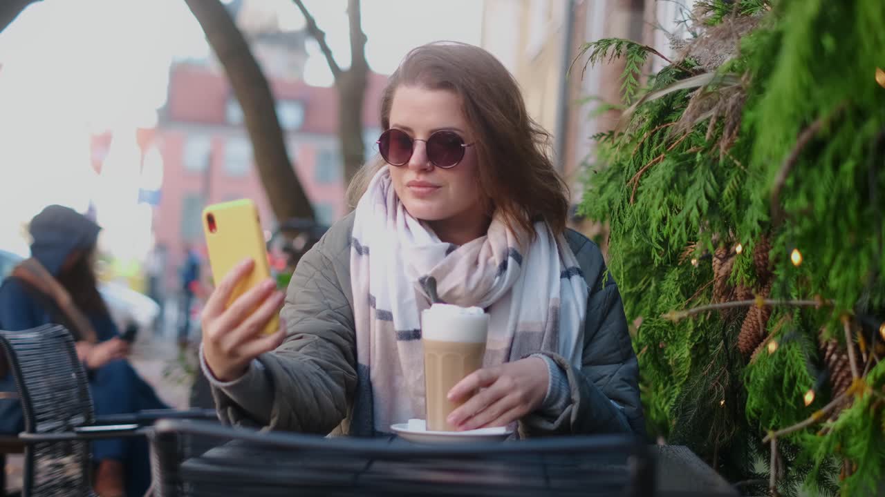 Kvinde tager en selfie på en hyggelig udendørs café, mens hun nyder en latte