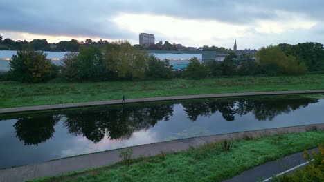 Low-angle-descend-to-the-bank-of-a-still-River-Exe-near-Exeter-St-David's-Railway-station-in-the-Autumn-with-an-unrecognised-person-on-an-early-morning-walk