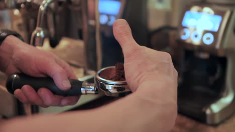 Scraping-off-excess-espresso-powder-on-a-portafilter,-slow-motion-close-up