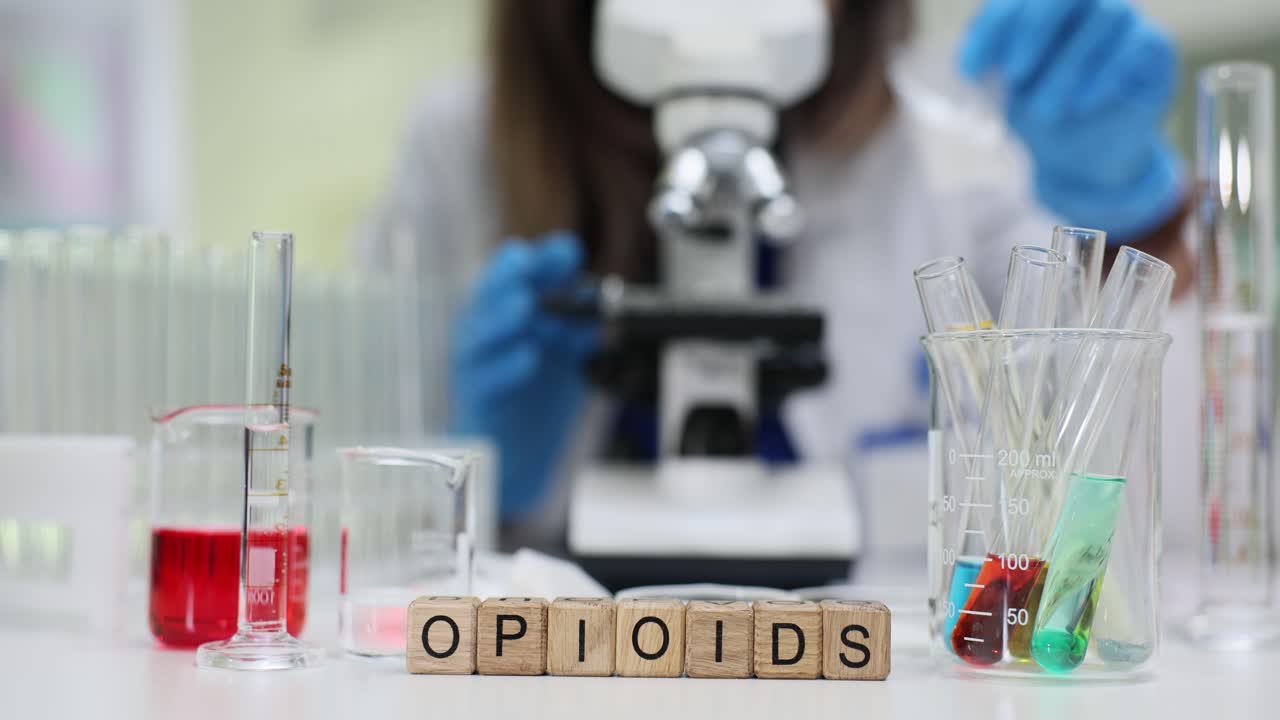Blocchi con la parola 'Oppioidi' su un tavolo da laboratorio con scienziato che conduce ricerche