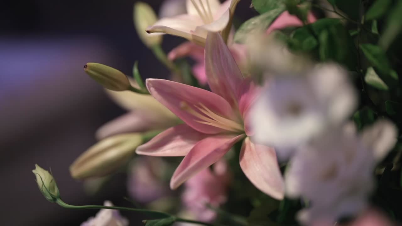 Primo piano cinematografico di gigli rosa freschi e fiori bianchi in un'elegante composizione centrotavola per matrimonio