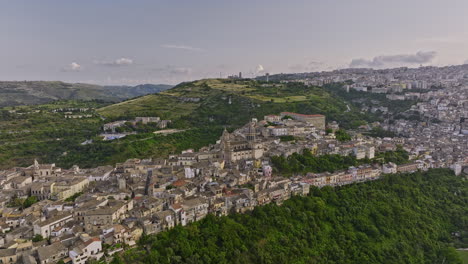 Ragusa-Italia-Vista-Aérea-V3-Vista-Panorámica-Drone-Sobrevolando-El-Valle-Alrededor-De-La-Histórica-Ciudad-De-Ibla,-En-La-Ladera-De-Una-Colina,-Capturando-La-Iglesia-Catedral-Del-Duomo-Di-San-Giorgio-Ubicada-Dentro---Filmada-Con-Cine-Mavic-3---Junio-De-2023