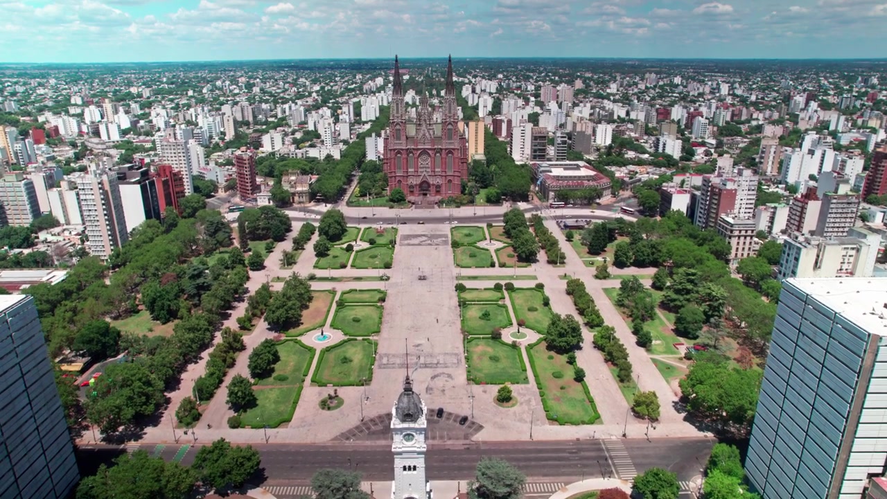 Ripresa aerea con drone in avvicinamento che vola in avanti sopra la torre dell'orologio del municipio attraverso Plaza Moreno verso le guglie neogotiche della Cattedrale di La Plata a La Plata, Argentina