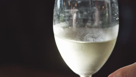 a hand gently lifts a cold white wine glass from a table in a dimly lit, elegant setting. side lighting highlights condensation and clarity