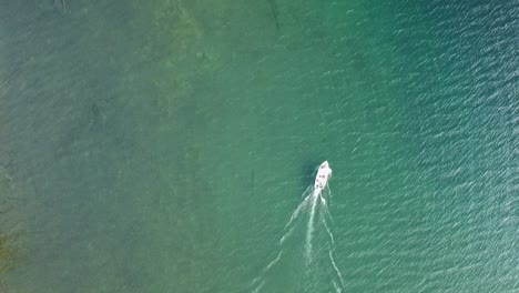 vista aérea de un avión teledirigido de un barco que corta lentamente las hermosas aguas de un lago cristalino con tonos esmeralda y azul en las zonas rurales del norte de canadá
