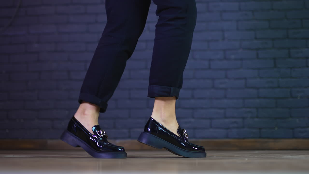 Female model's legs wearing blue fashionable jeans and low-heeled shoes. Black shining shoes decorated with massive silver chain demonstration.