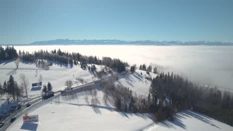 Sea-of-Clouds-above-Road-and-Stunning-Mountains-Landscape-in-Winter-Sunny-Day,-4k-Drone-Shot