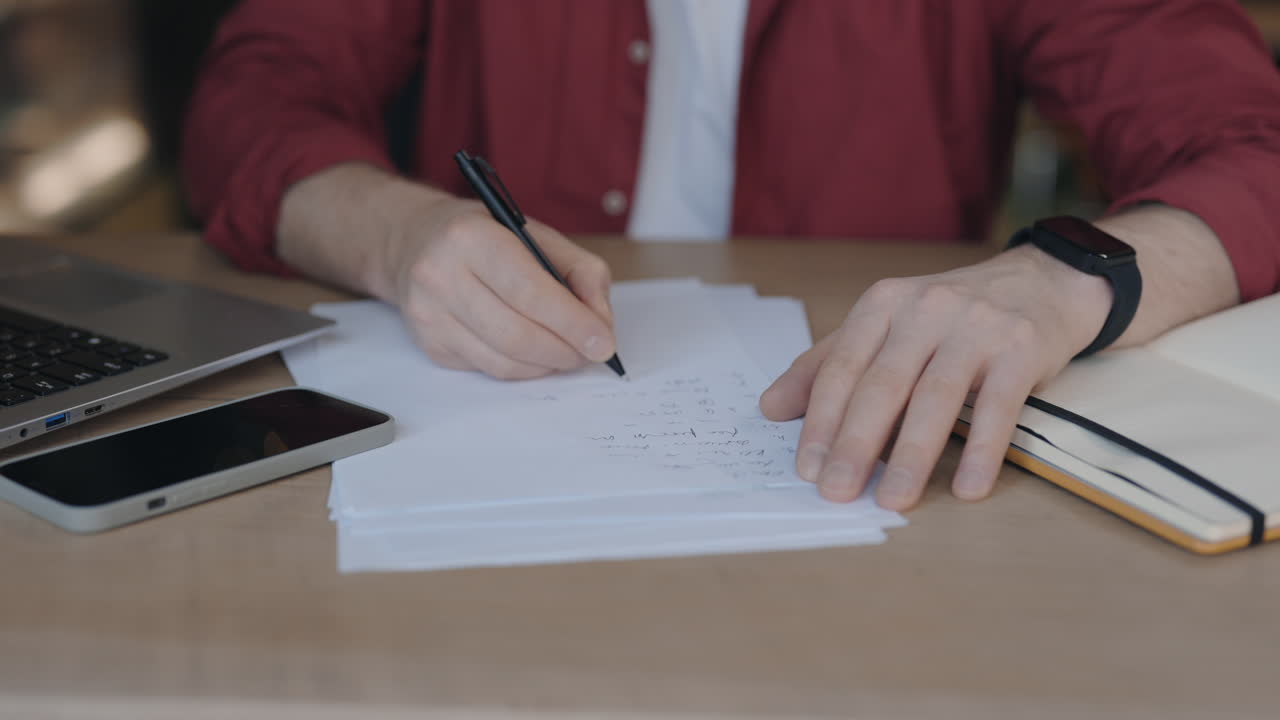 Man writing notes at a desk with a laptop and smartphone
