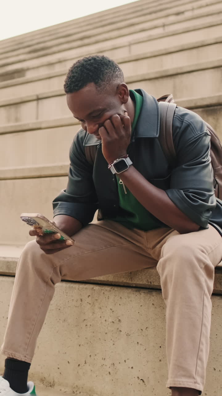 Young Man Sitting on Steps and Smiling While Using Smartphone