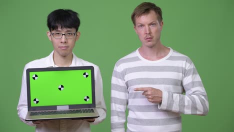 two young multi-ethnic businessmen showing laptop to the camera while pointing finger