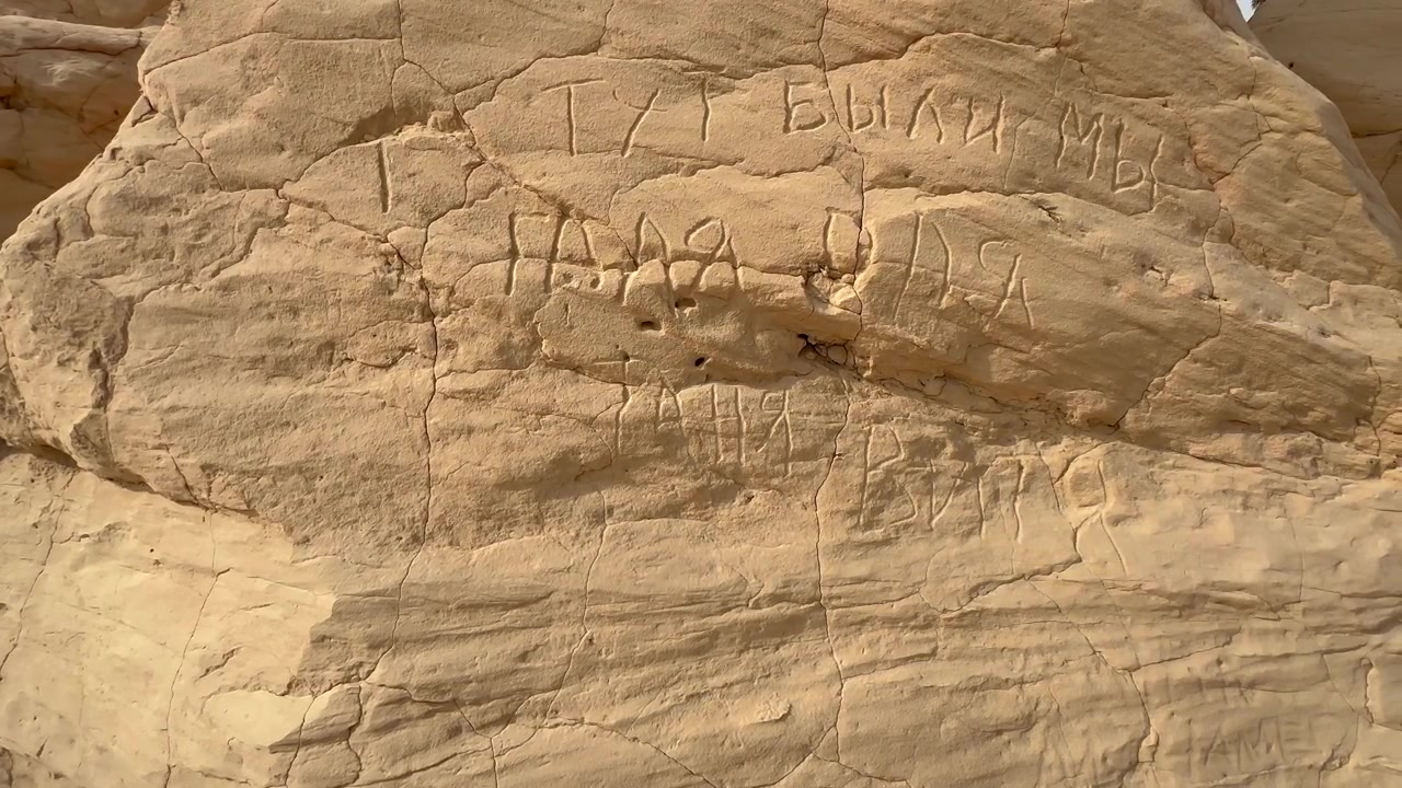 Close-up of Russian words carved into a light sandstone rock face in Debabcha, Tunisia, for use in travel or vandalism themes.