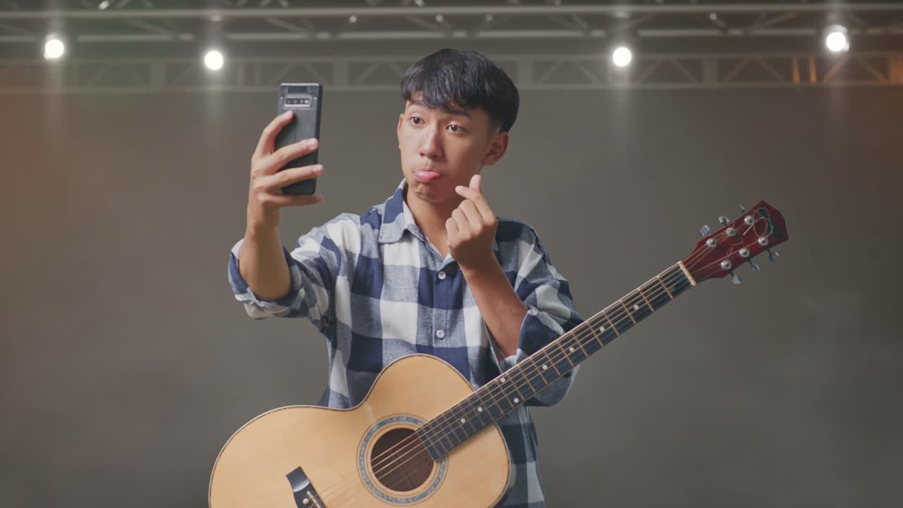 무대에 서 있는 스마트폰에서 기타 셀피를 찍은 아시아 십대