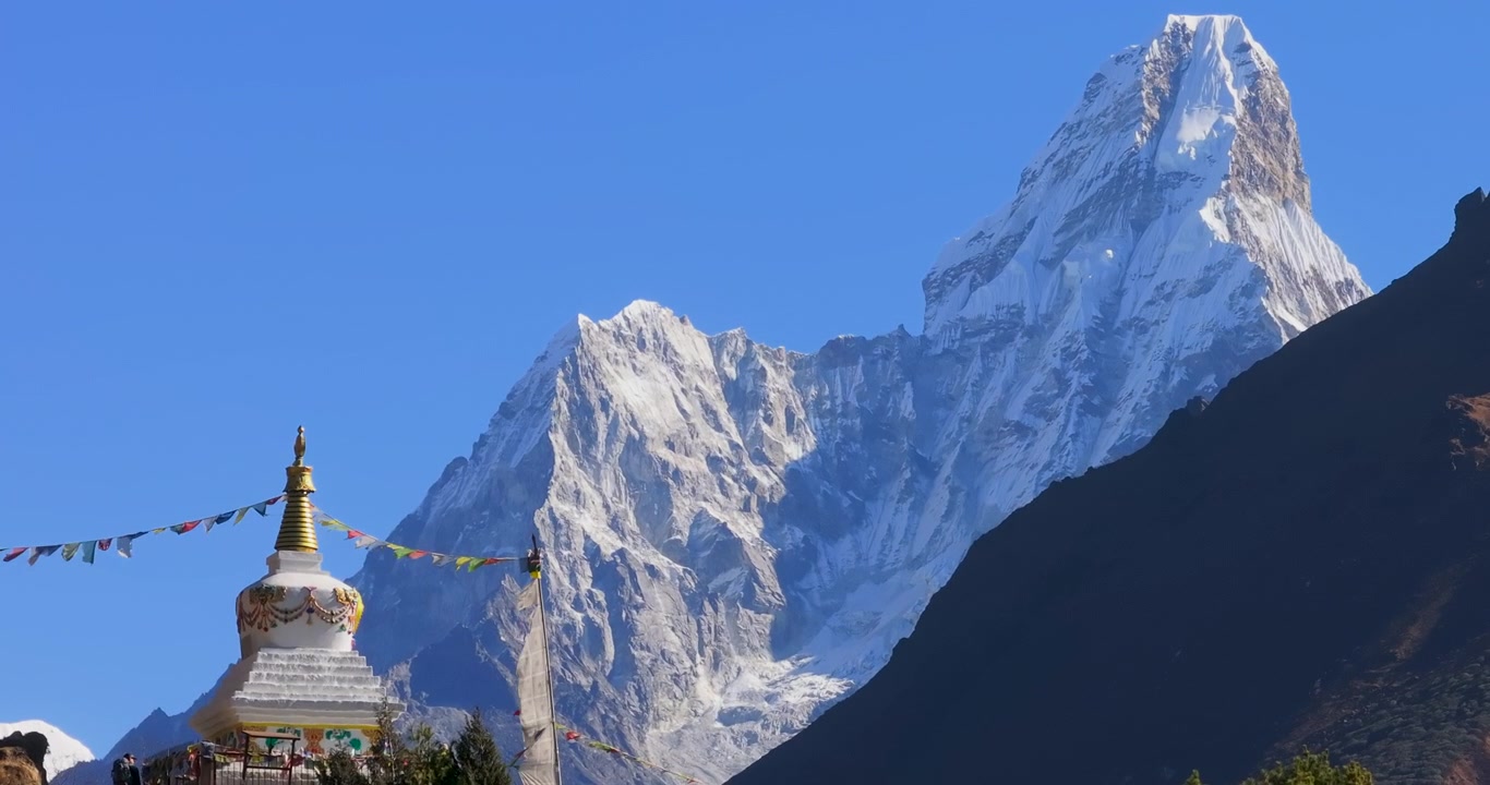 Namche Bazaar, Nepal, cảnh quay tĩnh rộng về đỉnh núi Ama Dablam phủ tuyết mang tính biểu tượng vươn lên phía sau một bảo tháp Phật giáo truyền thống với cờ cầu nguyện và sườn đồi trước khung cảnh núi non.