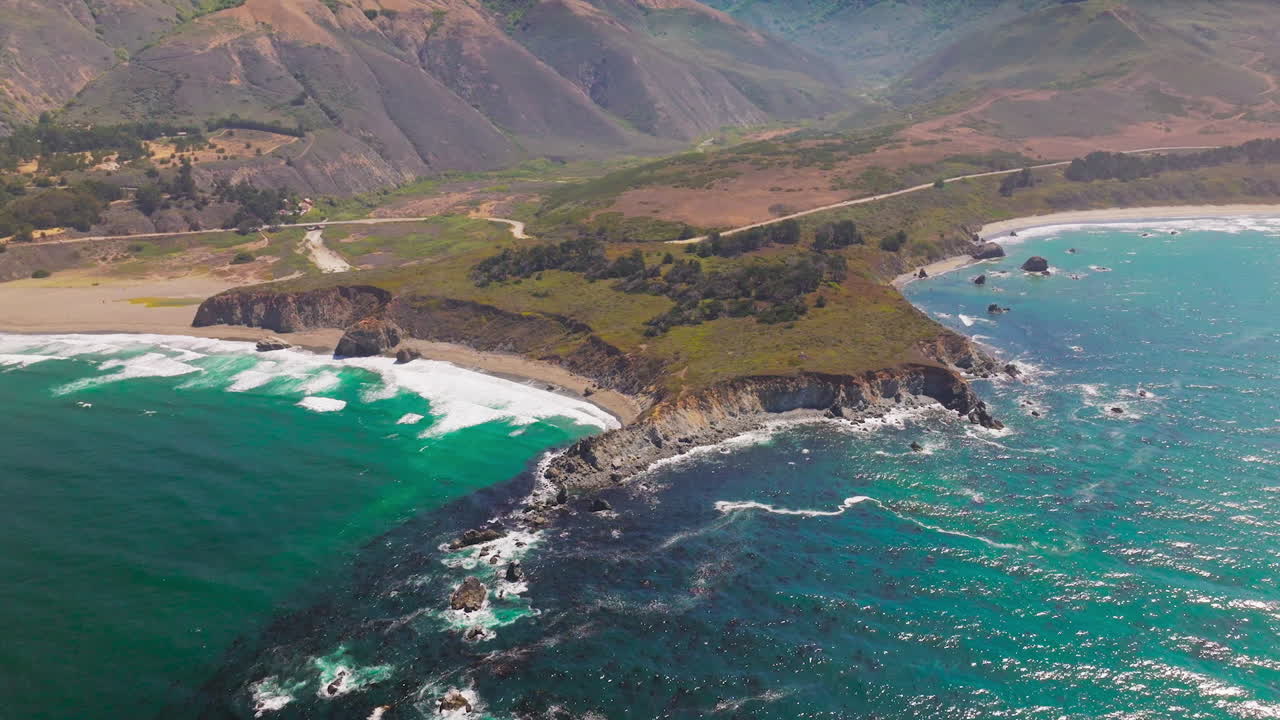 Craggy shore of the Pacific Ocean at Morro Bay, California, USA. Bare brown mountains at backdrop. Aerial perspective.